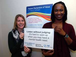 Two staff holding a sign reading: Listen without judging: it’s hard to open up when you may have a mental health need.
