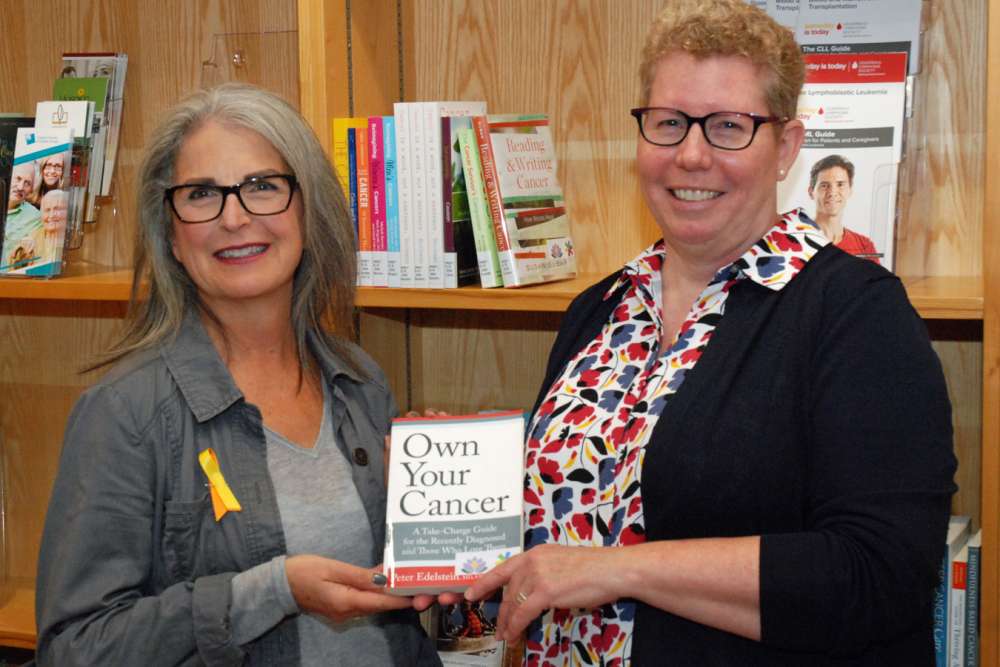 Two people holding a book in the cancer centre's resource centre