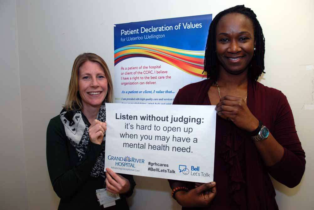 Two staff holding a sign reading: Listen without judging: it’s hard to open up when you may have a mental health need.
